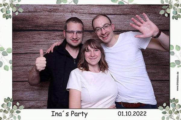 Das Bild zeigt drei Gäste, die mit einem breiten Lächeln und lockerer Stimmung vor dem rustikalen Fotobox-Hintergrund posieren. Aufgenommen bei Ina’s Party im Hotel Schloss Lichtenwalde, steht dieses Bild für authentische Erinnerungen und gemeinsame Freude. Fotobox für Feier im Hotel Schloss Lichtenwalde mit drei lachenden Gästen