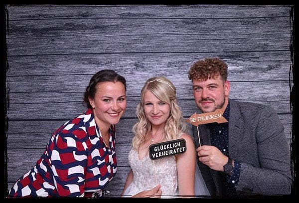 Brautpaar und Gäste posieren mit lustigen Schildern in der Fotobox auf einer Hochzeit in Sachsen.