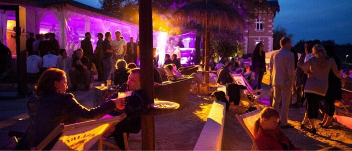 Stimmungsvoll beleuchtete Eventlocation mit Gästen, die sich in entspannter Atmosphäre unterhalten – perfekt für unvergessliche Fotos für Events.