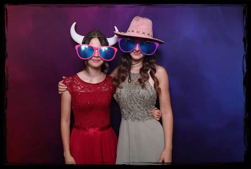 Zwei Gäste mit lustigen Accessoires vor der Fotobox auf einer Hochzeit.
