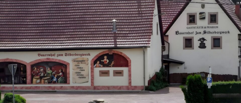 Frontansicht des Bauernhofs zum Silberbergwerk mit detailreicher Fassadenmalerei und historischer Schrift.