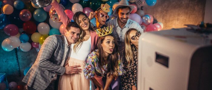 Gruppe feiernder Menschen posiert vor einer Fotobox mit buntem Ballon-Hintergrund – perfekt für Audiogästebuch und Fotobox auf Events