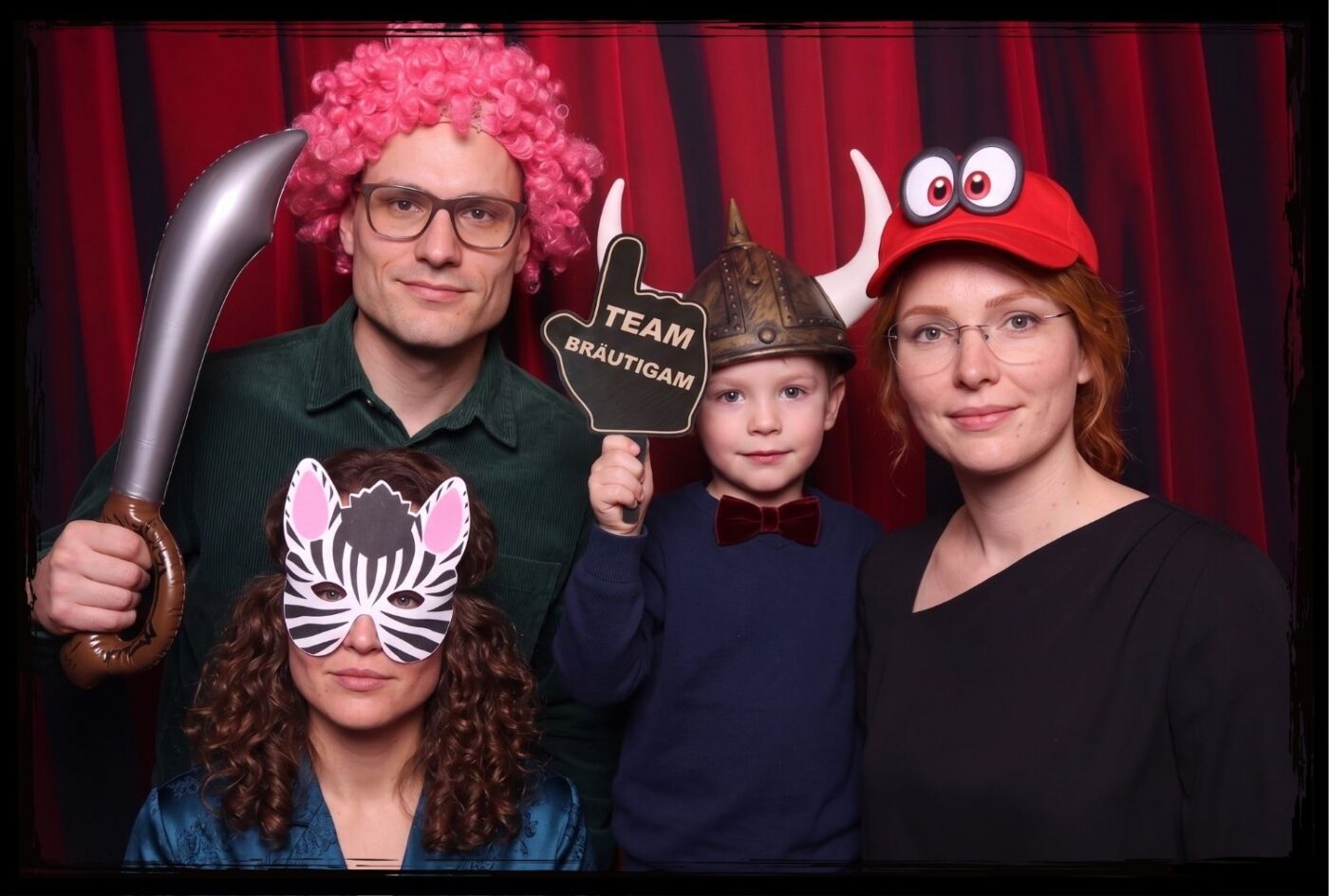 Gruppe mit Brille und Wikingerhelm hält ein Team Bräutigam Fotobox Schild