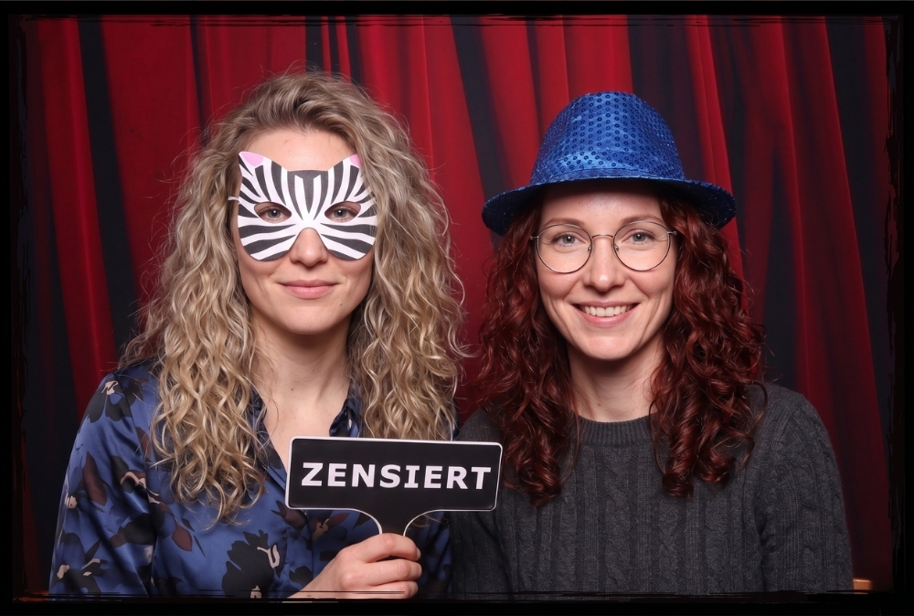 Zwei Frauen mit Zensiert-Schild und Maske in der Fotobox