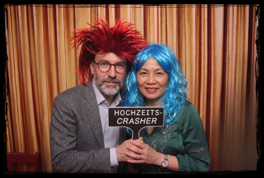 Cooles Fotobox Motiv Hochzeits-Crasher Paar mit Hochzeits-Crasher Schild und Perücken vor der Fotobox
