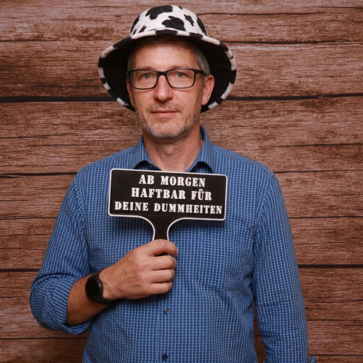 Mann mit Kuhhut hält mit ernstem Gesicht das Fotobox Schild Ab morgen haftbar für deine Dummheiten in die Kamera