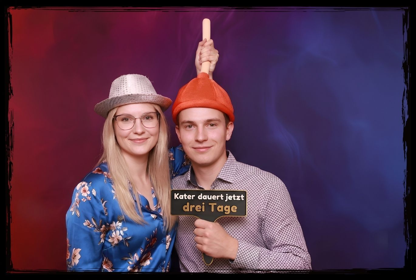 Junges Paar posiert mit bunten Partyhüten und einem Fotobox Schild zum 30. Geburtstag mit dem Text Kater dauert jetzt drei Tage