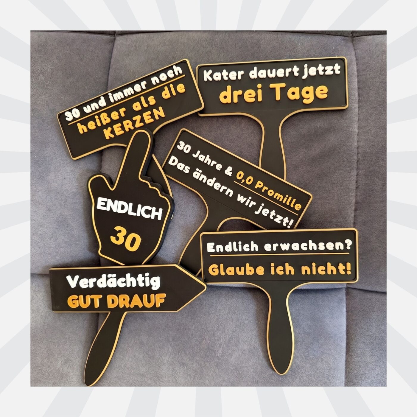Alle sechs Fotobox Schilder zum 30. Geburtstag liegen nebeneinander auf einem grauen Sofa